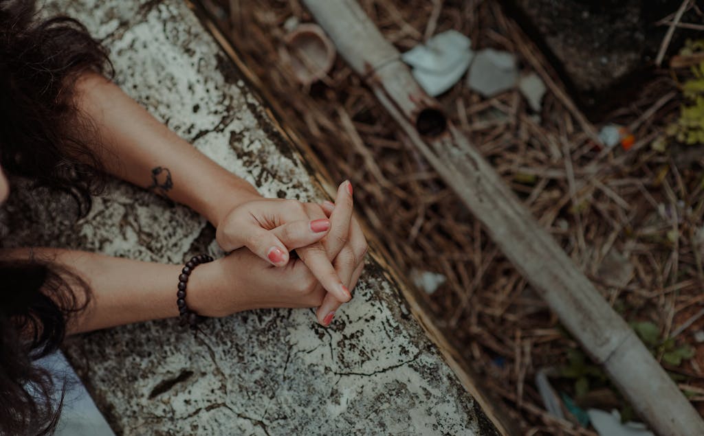 Close-up shot of hands with bracelet and tattoo on weathered surface, showcasing earthy tones.
