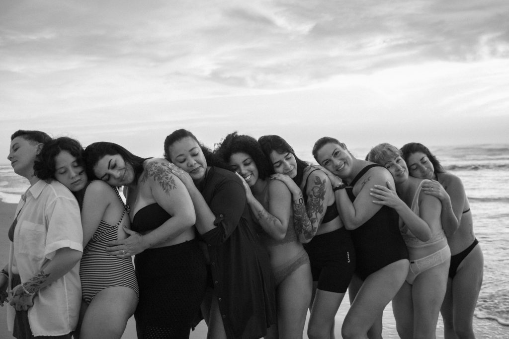 A diverse group of women embraces on Tramandaí Beach, showcasing friendship and body positivity.